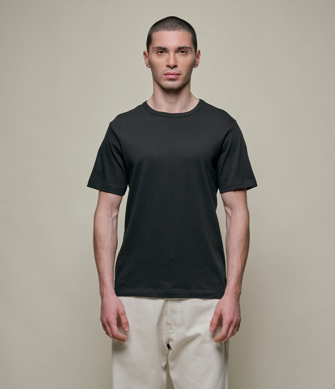 Man wearing a black t-shirt and beige pants against a plain background