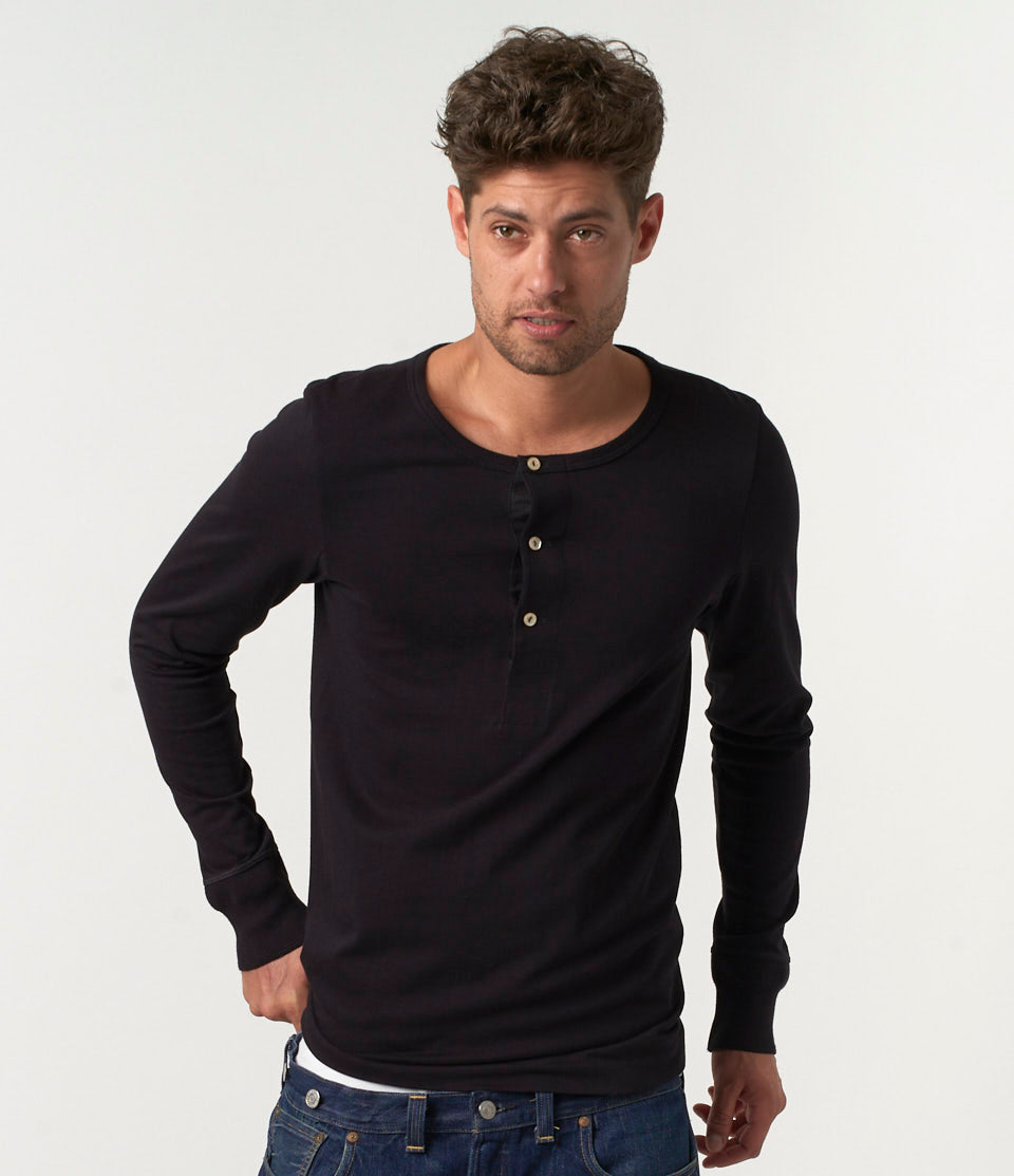 A man wearing a black long sleeve henley shirt with buttons at the neck area.