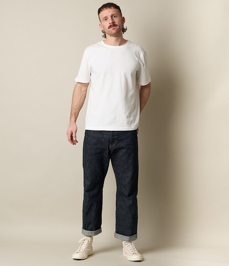 Man wearing a white t-shirt and dark blue jeans against a plain background