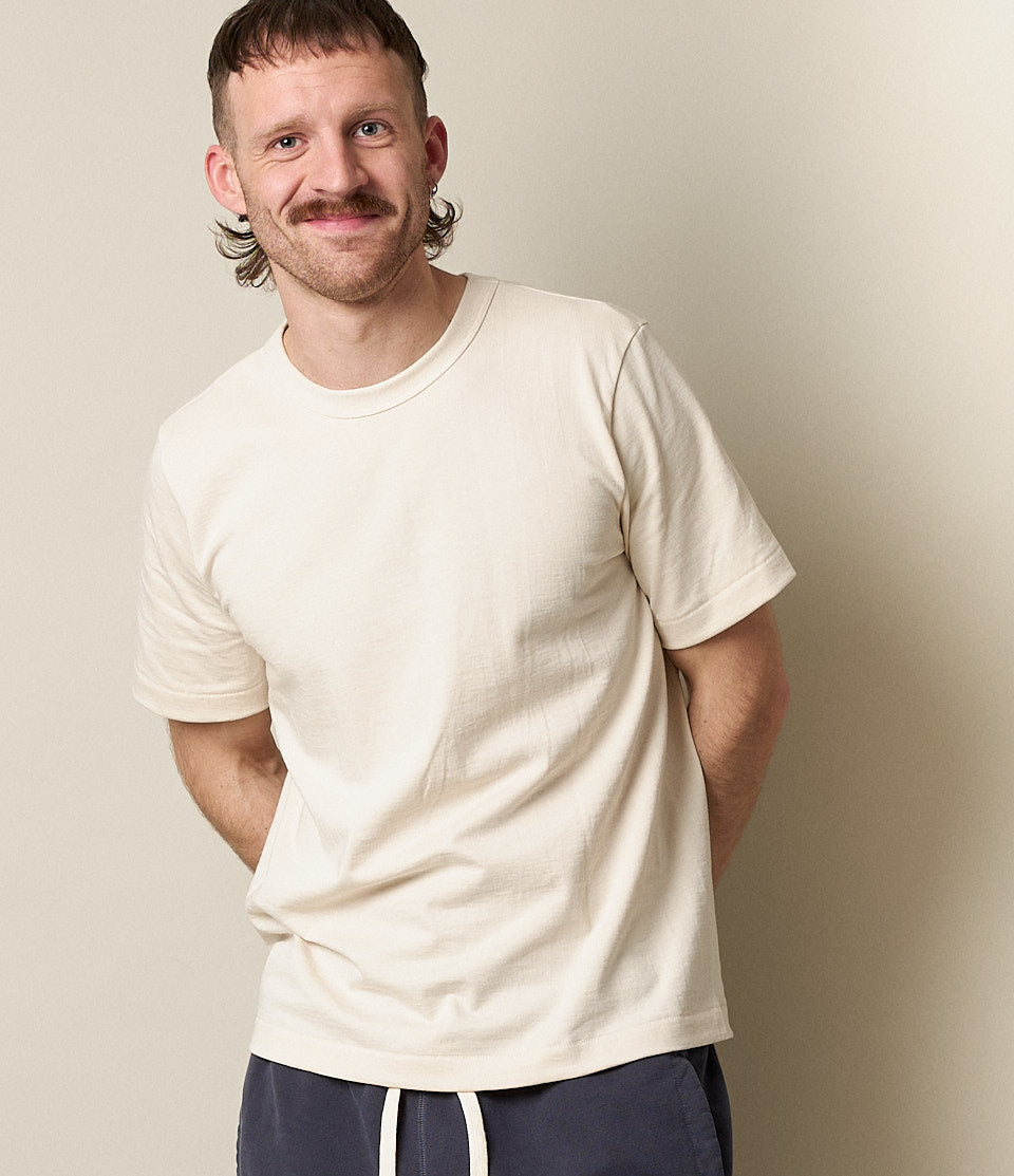 A man wearing a beige, short-sleeved, relaxed fit T-shirt with a round neckline.