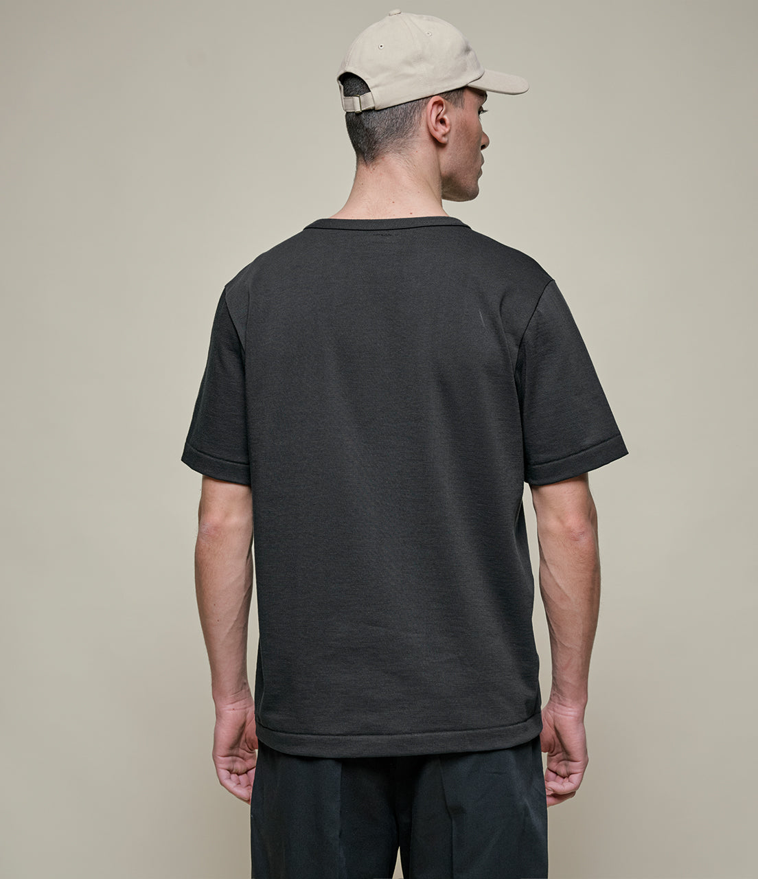 Man wearing a black t-shirt and beige cap on a plain background