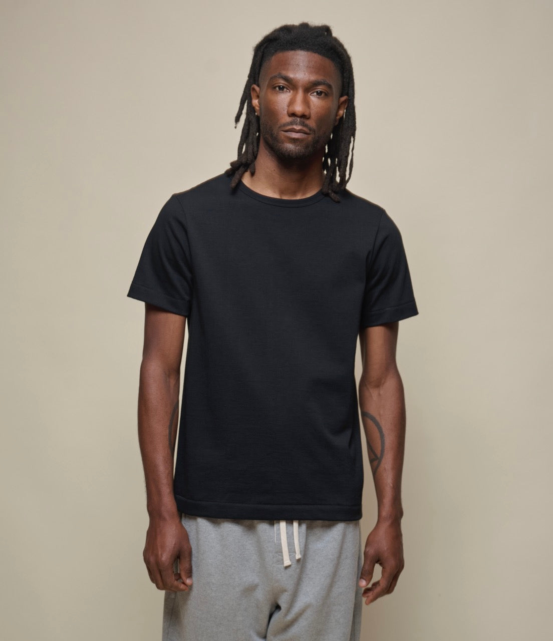 A person wearing a black loopwheeled, short-sleeved T-shirt with a round neck, paired with light-colored pants.