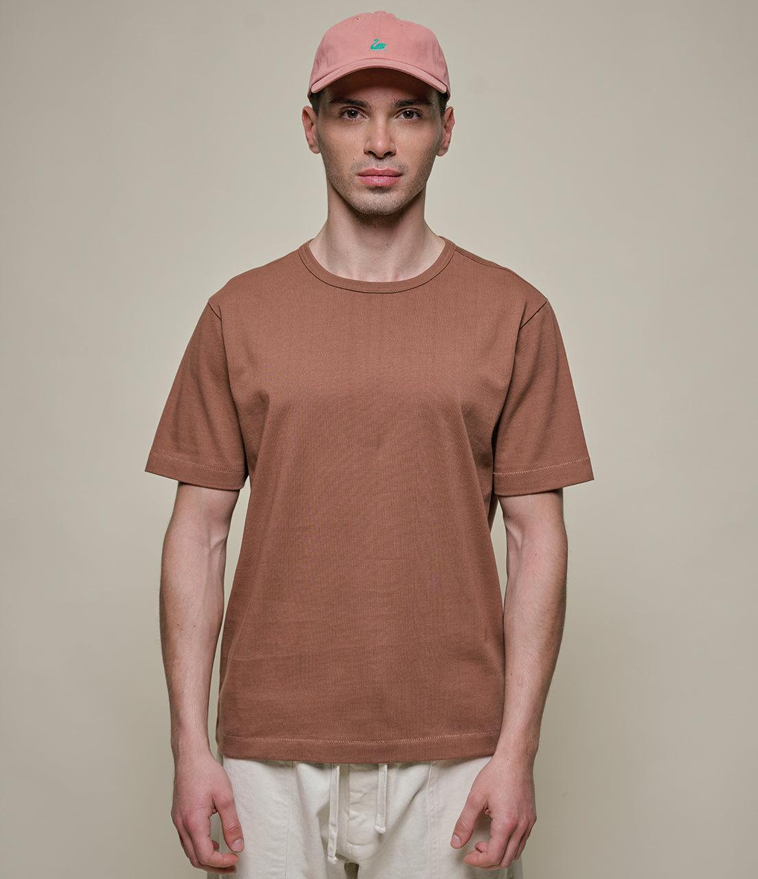 Man wearing a brown t-shirt and pink cap against a plain background