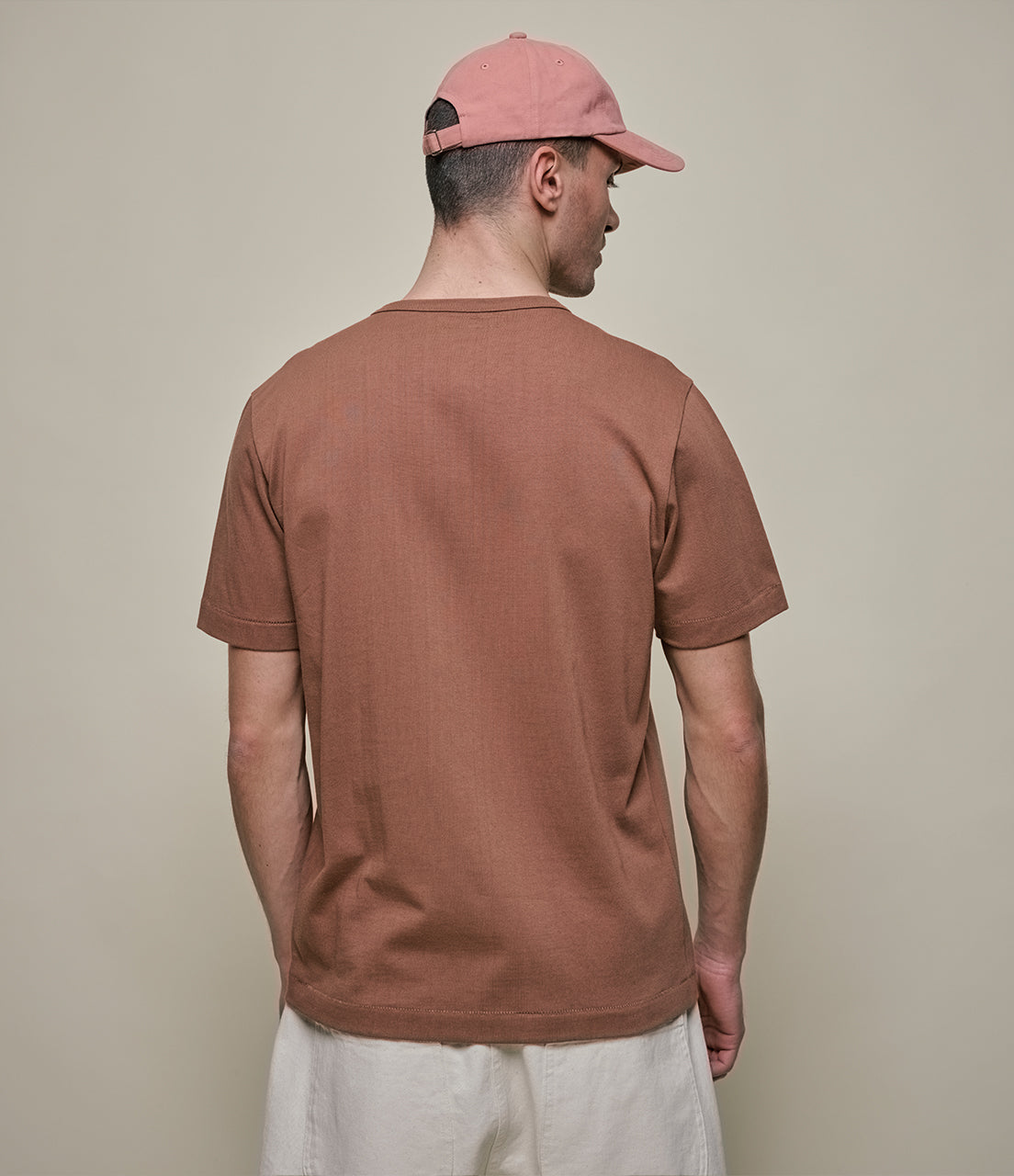 Man wearing a brown t-shirt and pink cap against a beige background