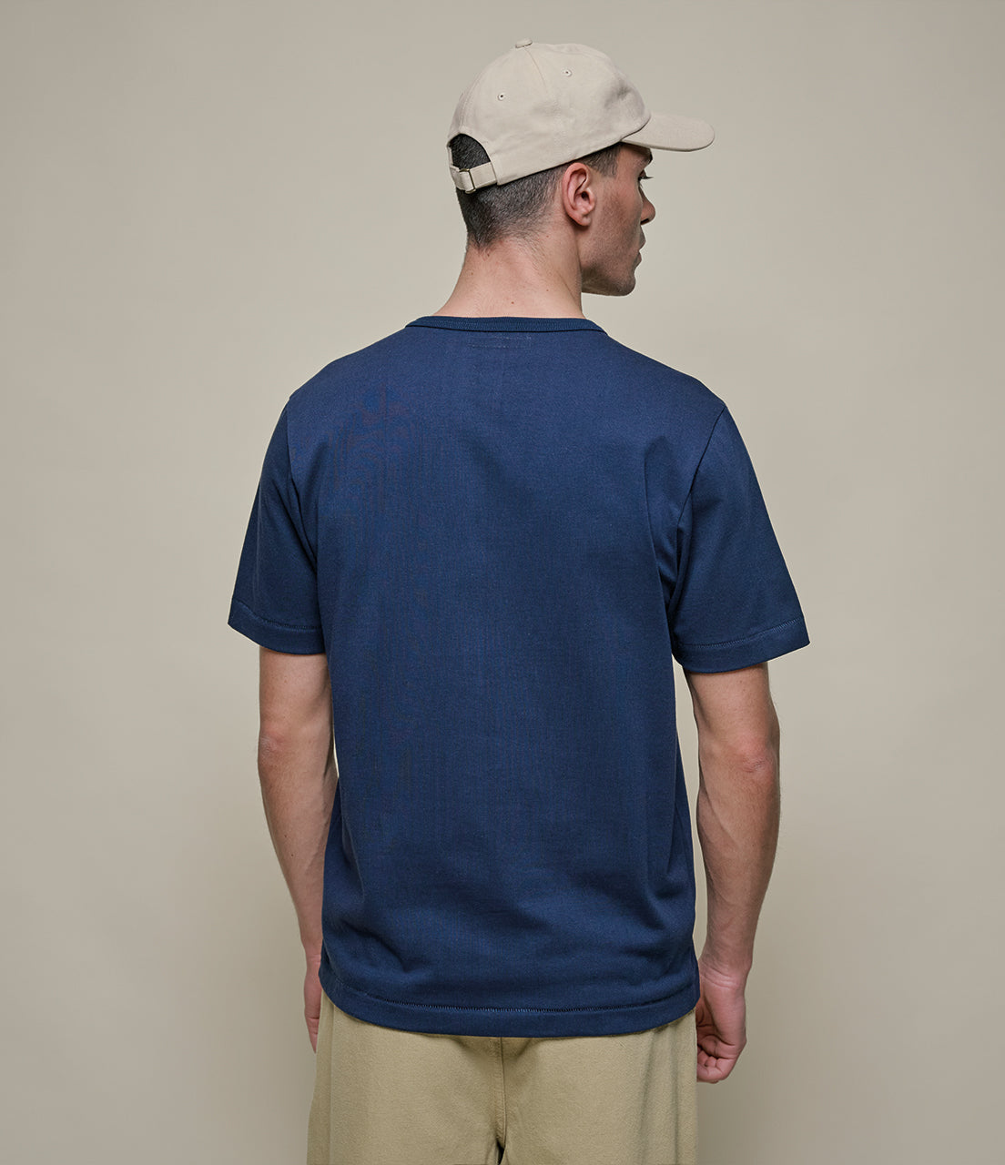 Man wearing a blue t-shirt and beige cap against a plain background