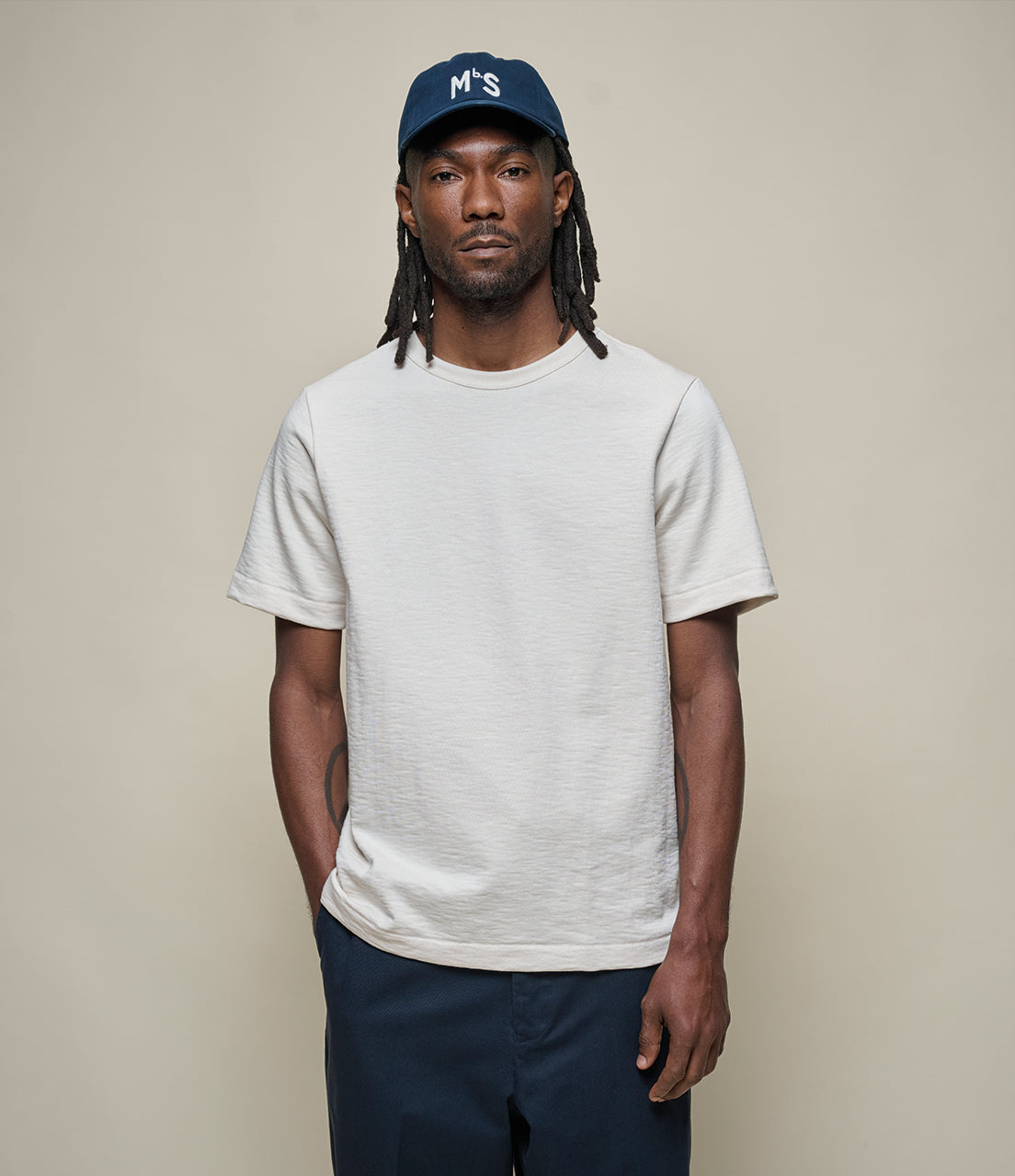 Man wearing a beige t-shirt and navy cap against a beige background