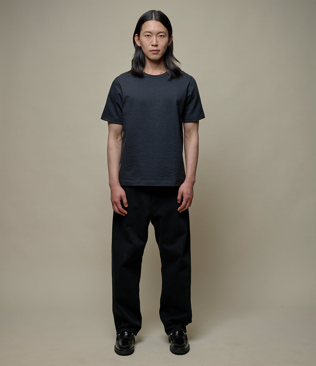 Person wearing a black t-shirt and pants on a beige background