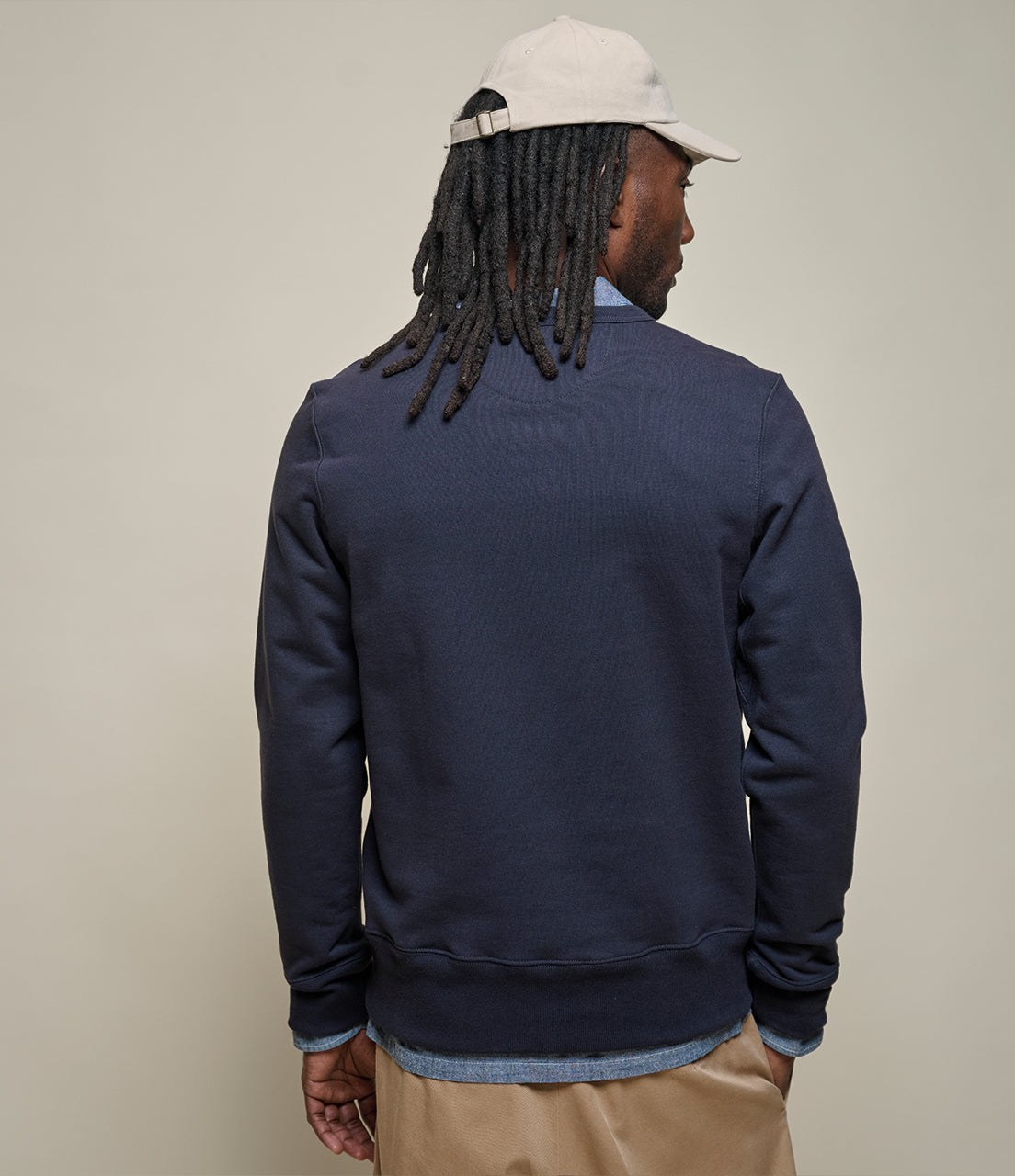 Man wearing a navy blue sweatshirt with a beige cap on a plain background