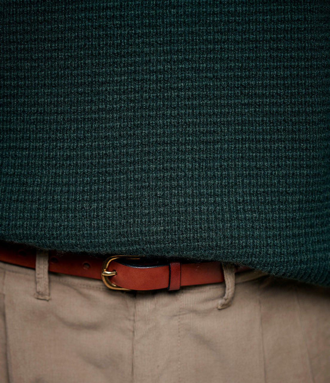 Close-up of a textured green jacket with a brown belt and beige pants.