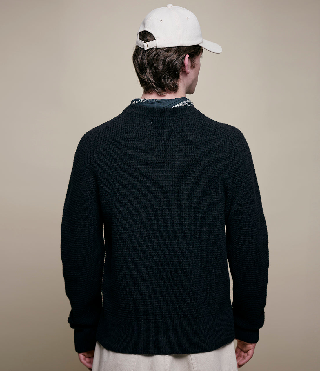 Person wearing a black sweater and white cap from behind on a beige background