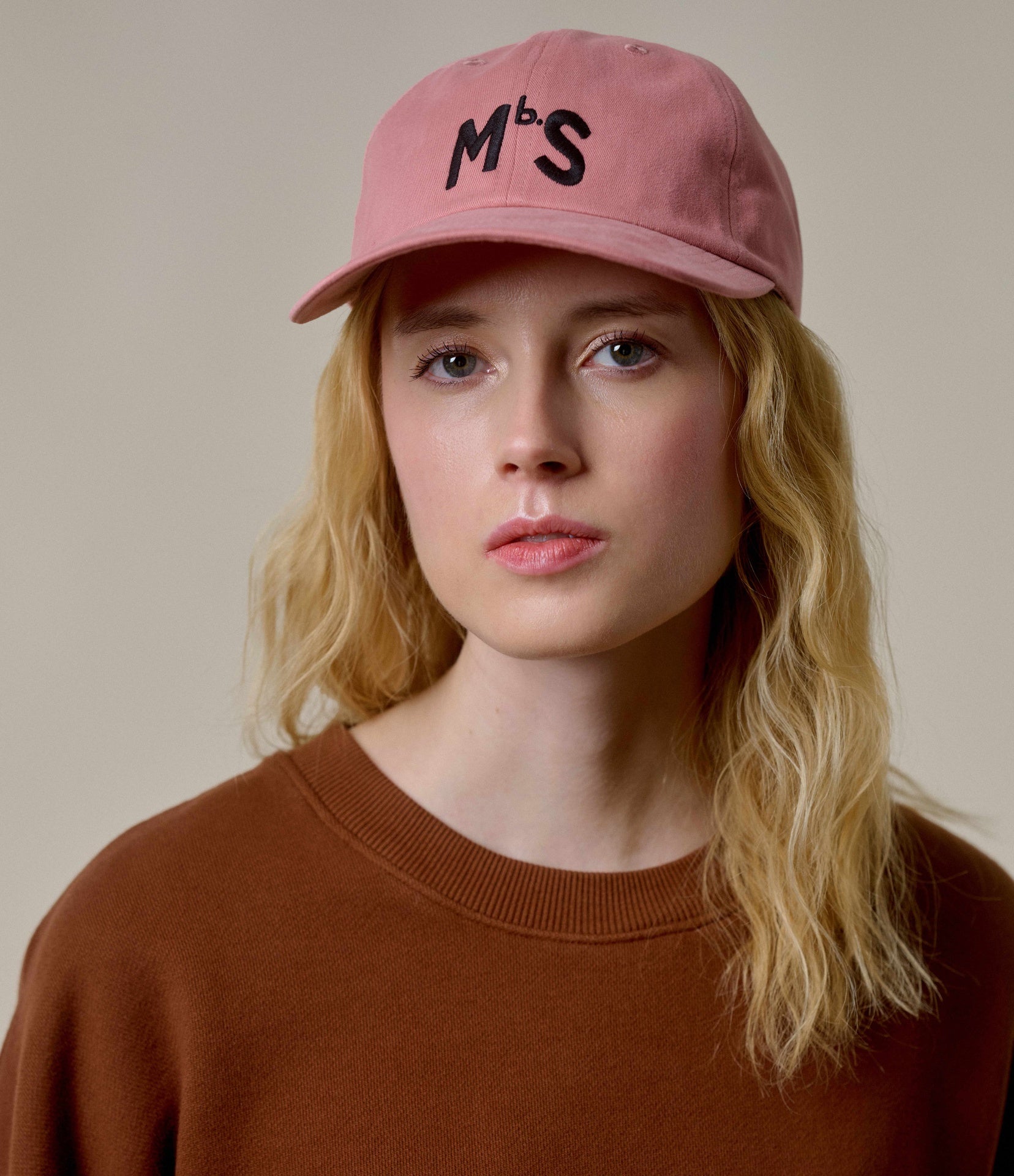 Woman wearing a pink cap with 'Mbs' logo against a neutral background