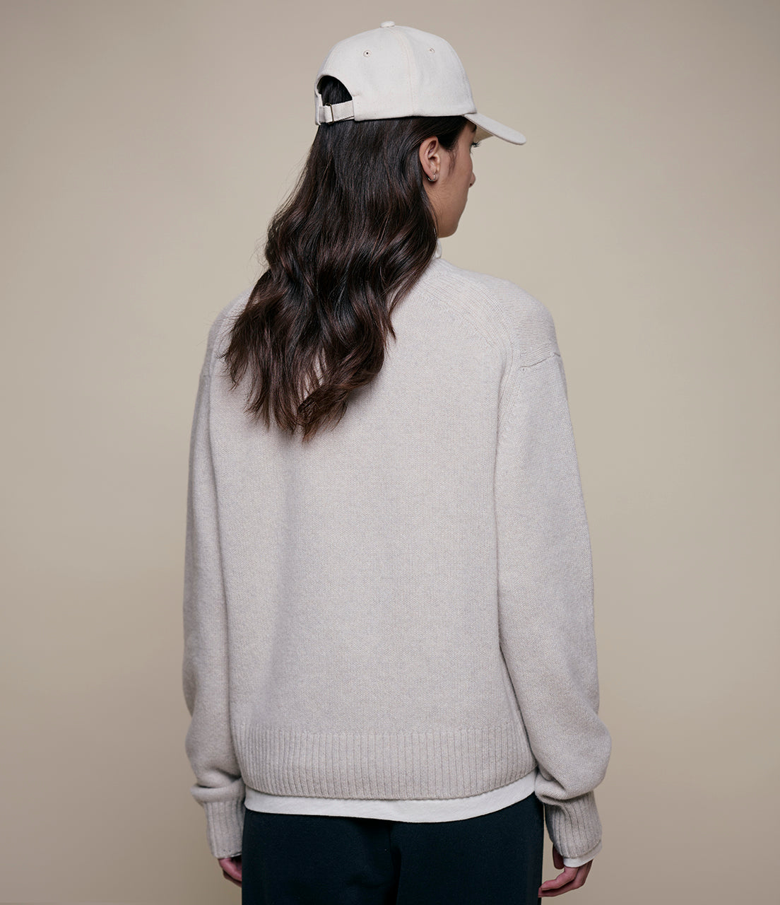 Person wearing a light gray sweater and white cap on a beige background
