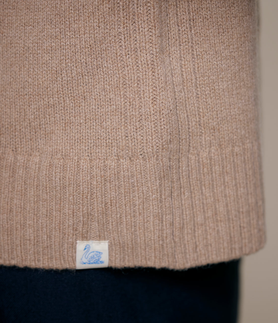 Close-up of a brown textured cashmere fabric with a brand label on a plain background