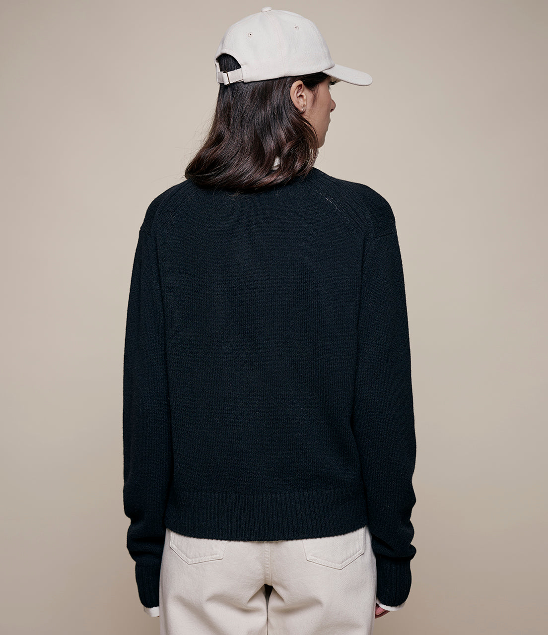 Person wearing a black sweater and white cap from behind on a beige background