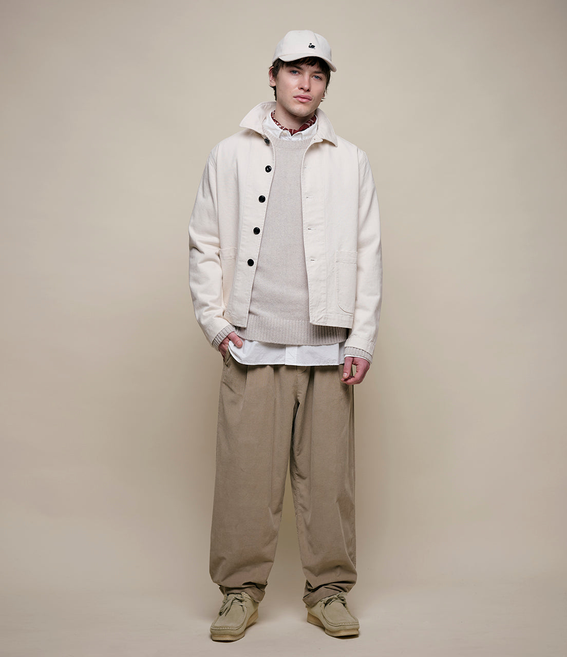 Person wearing a white jacket, beige pants, and a white cap on a plain background