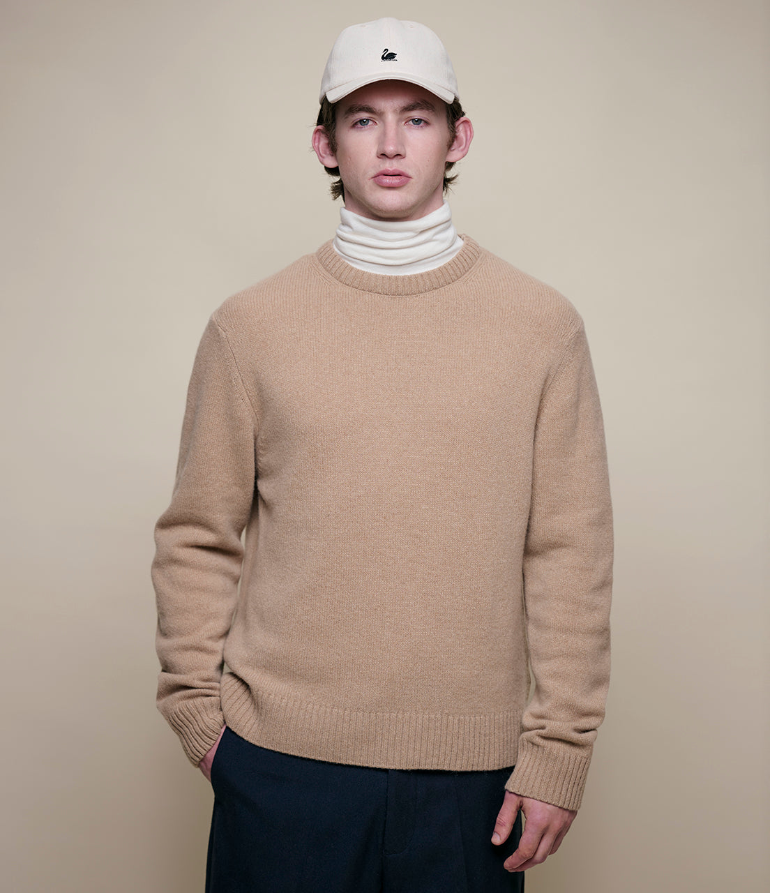 Man wearing a beige cashmere sweater and white turtleneck with a plain background