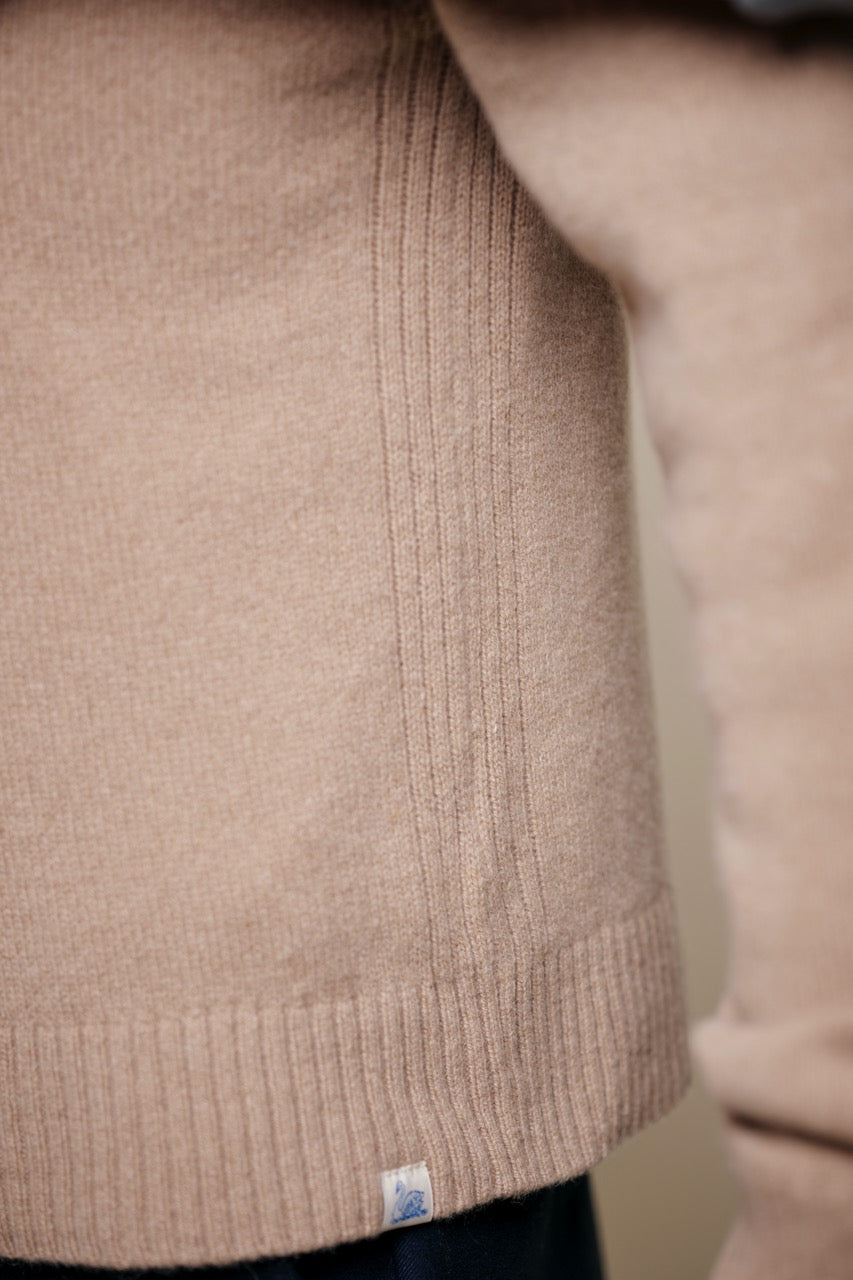Close-up of a beige cashmere sweater with a brand label on a neutral background