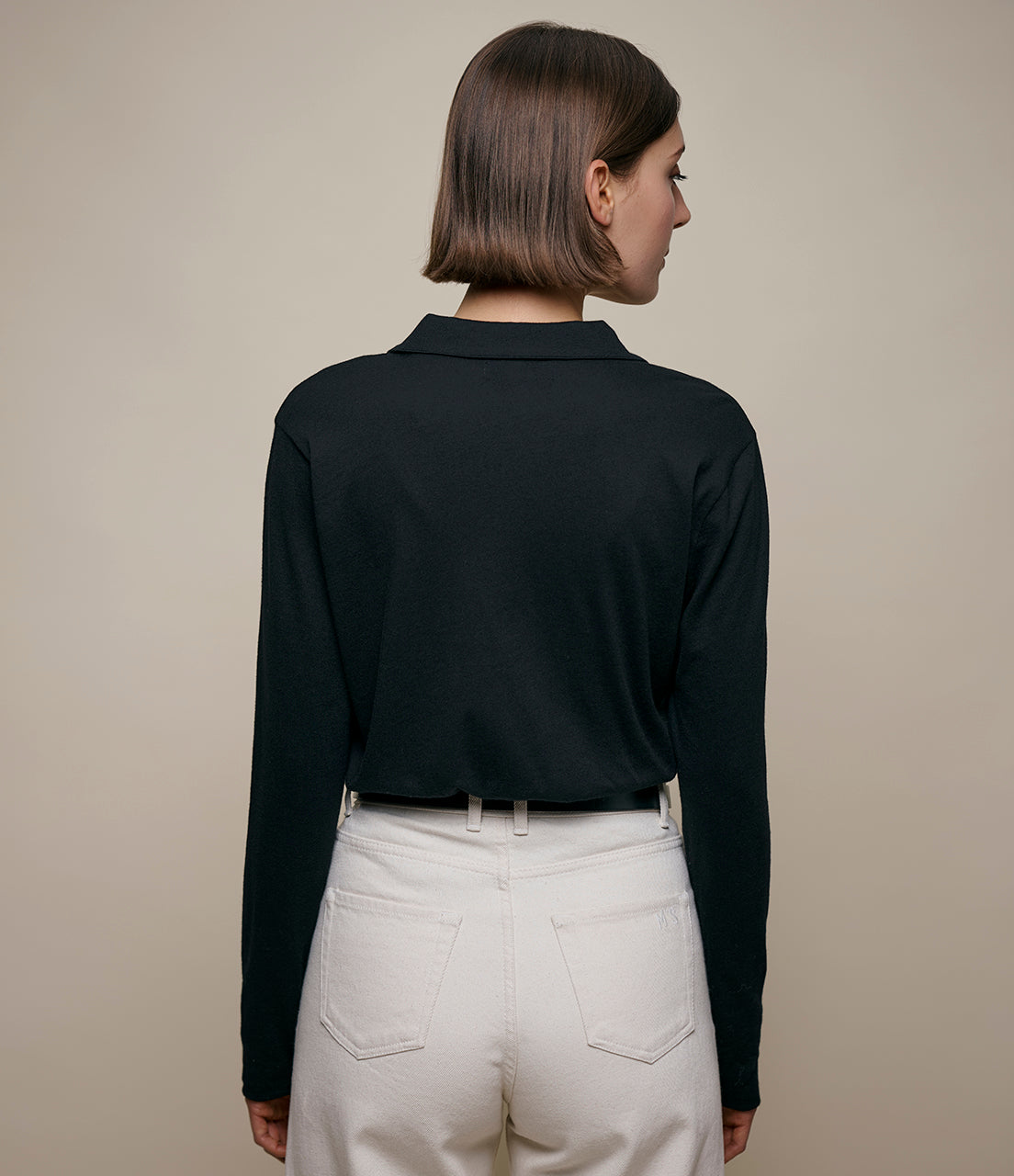 Person wearing a black long-sleeve shirt and beige pants against a beige background
