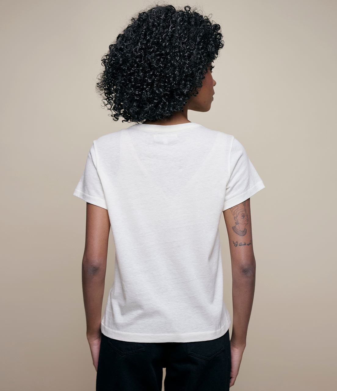 Person wearing a plain white t-shirt against a beige background