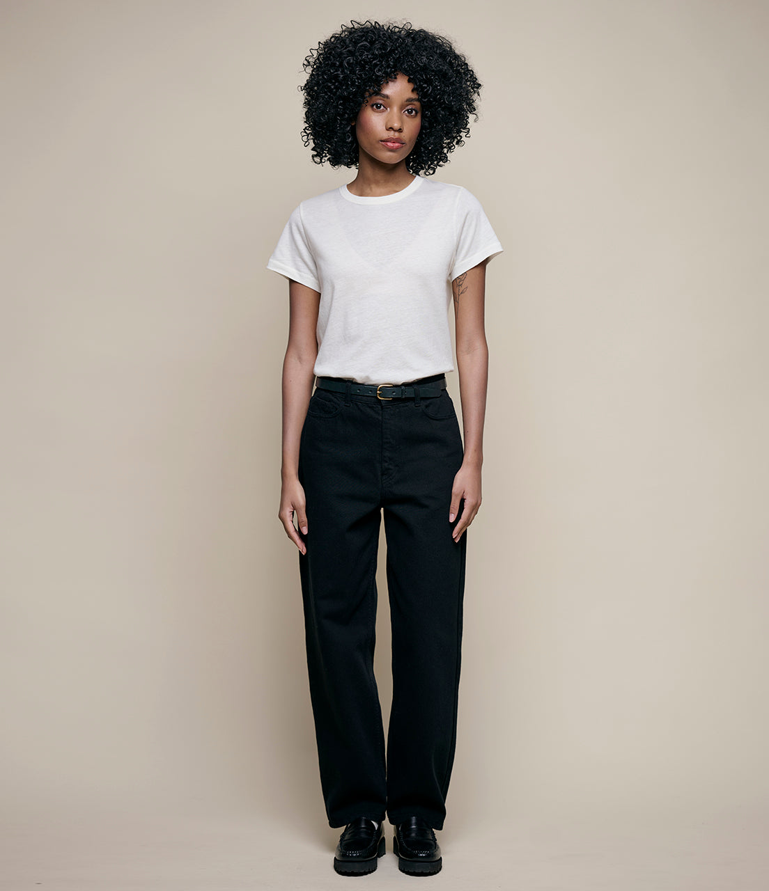 Person wearing a white t-shirt and black pants against a beige background