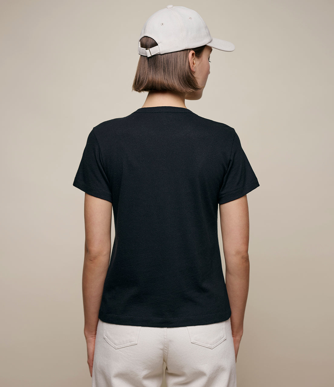 Person wearing a black t-shirt and white cap on a beige background