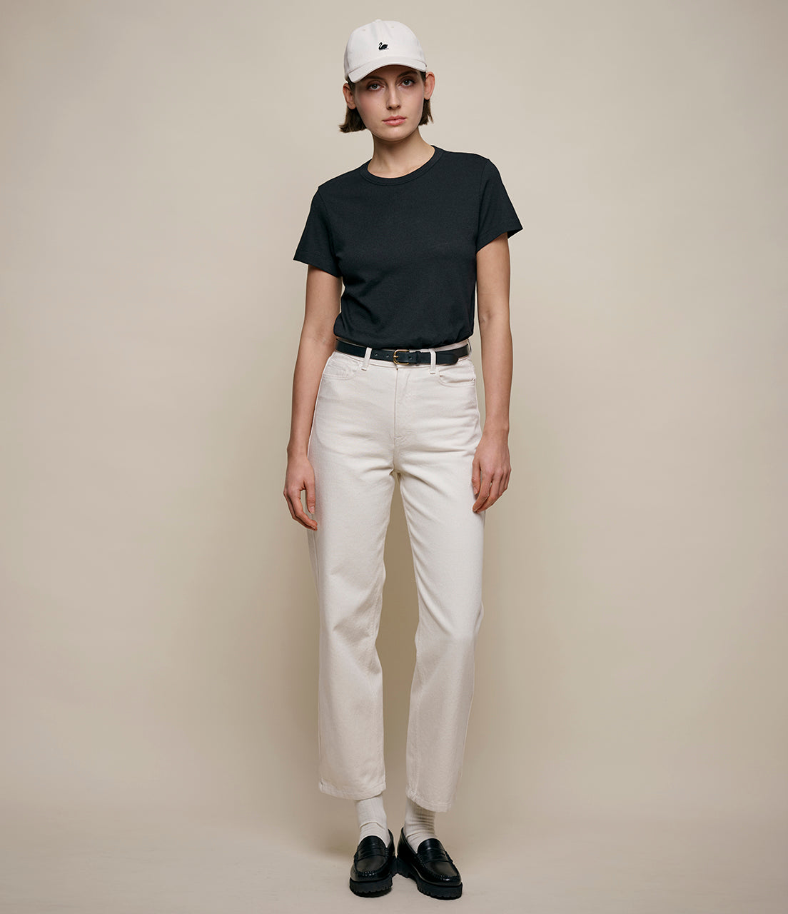 Person wearing a black t-shirt, white pants, and a white cap on a beige background