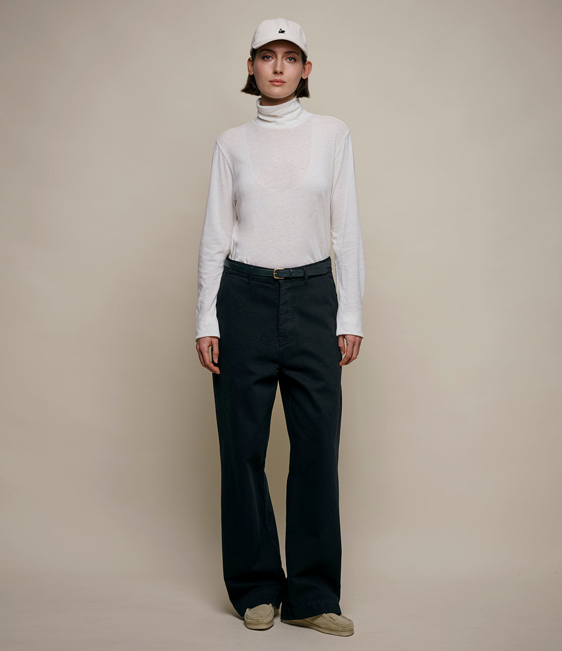 Person wearing a white turtleneck and black pants on a beige background