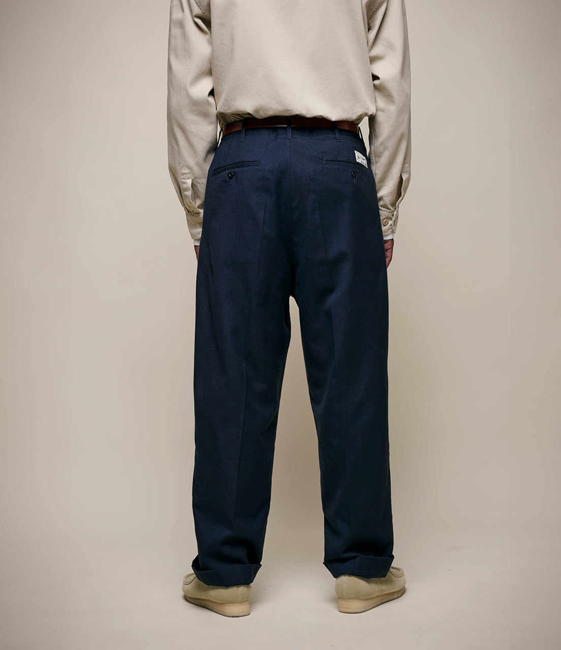 Person wearing a beige jacket and navy pants on a plain background