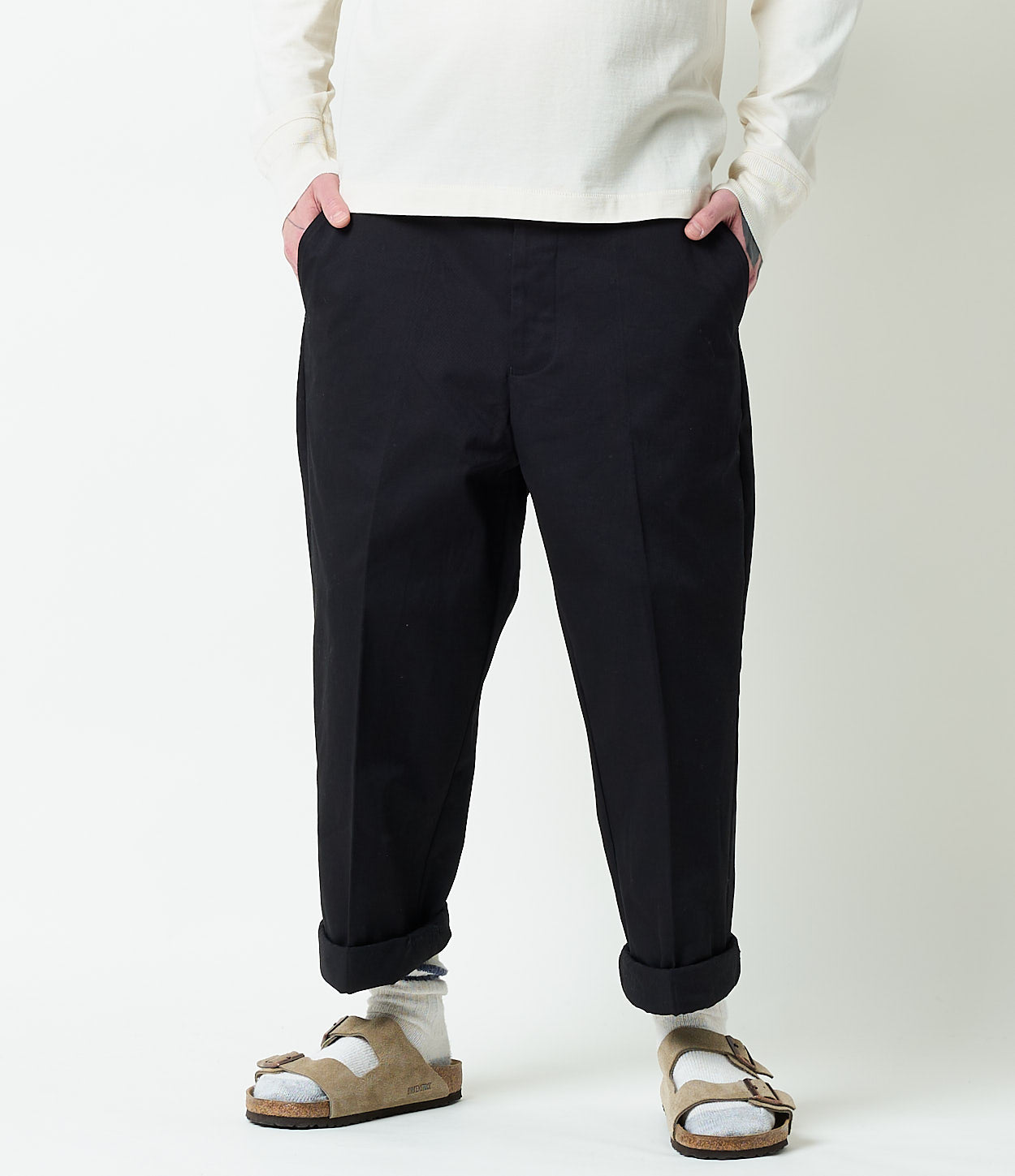 Person wearing dark navy chino pants and white sweater on a white background