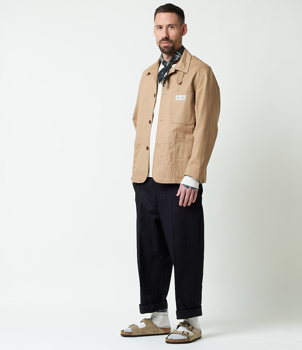 Man wearing a beige jacket and dark navy pants on a white background