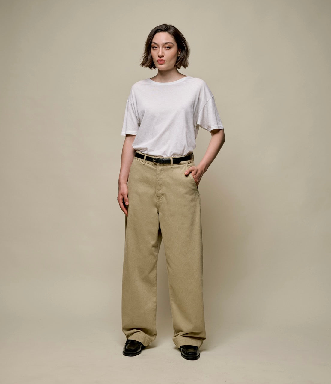 Woman wearing a white t-shirt and beige pants against a plain background