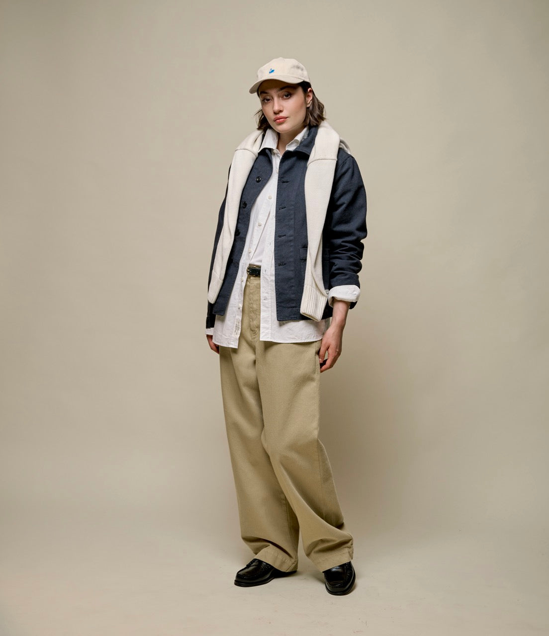 Person wearing a casual outfit with a vest, shirt, and pants on a plain background