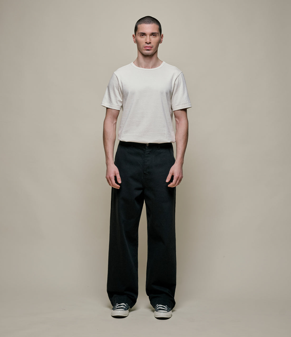 Man wearing a white t-shirt and black pants against a plain background