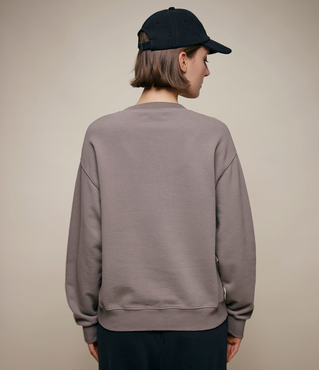 Person wearing a gray sweatshirt and black cap on a beige background