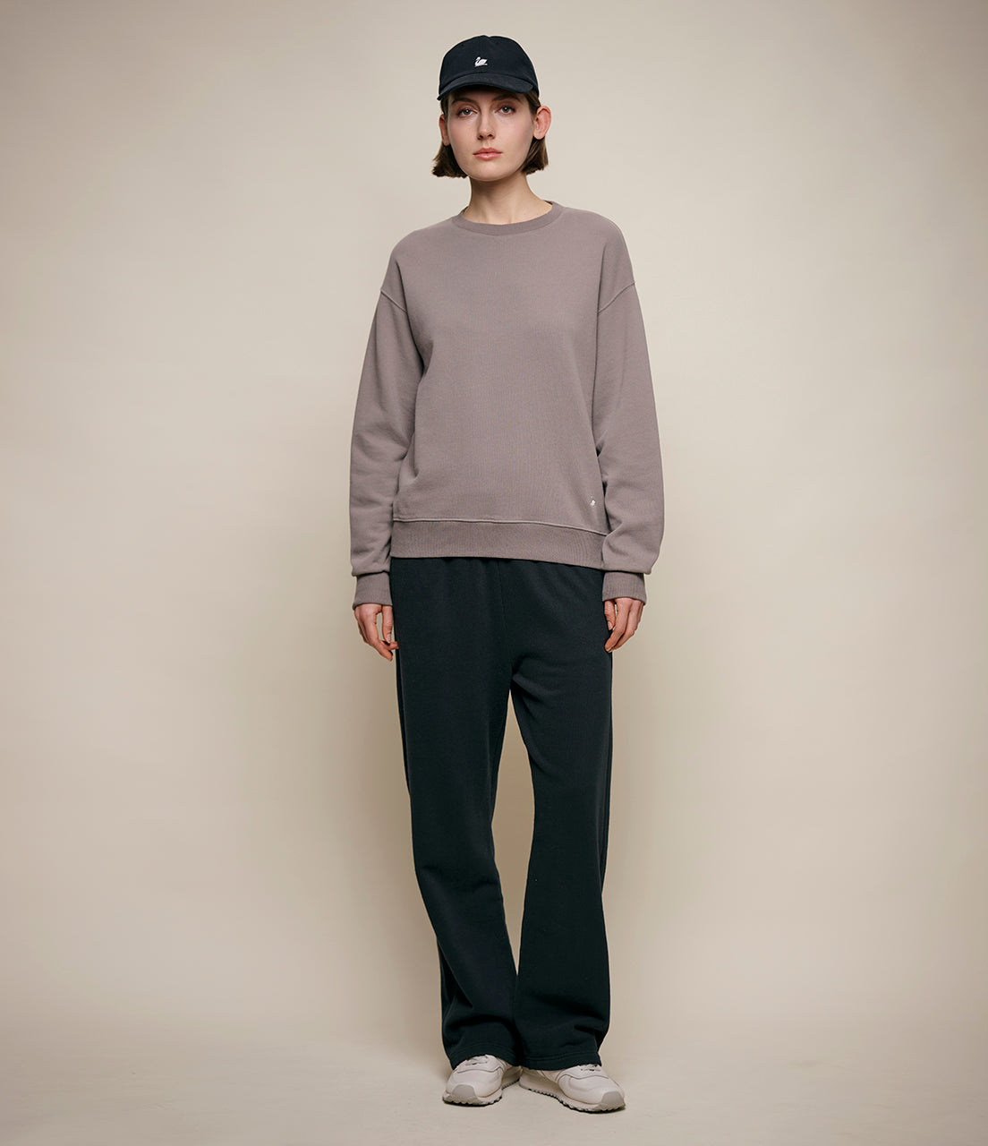 Person wearing a gray sweatshirt and black pants against a beige background
