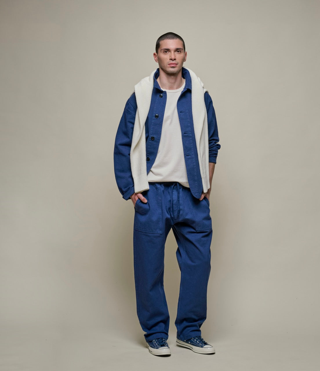 Man wearing blue cotton twill jacket and pants with a beige sweater around his shoulders