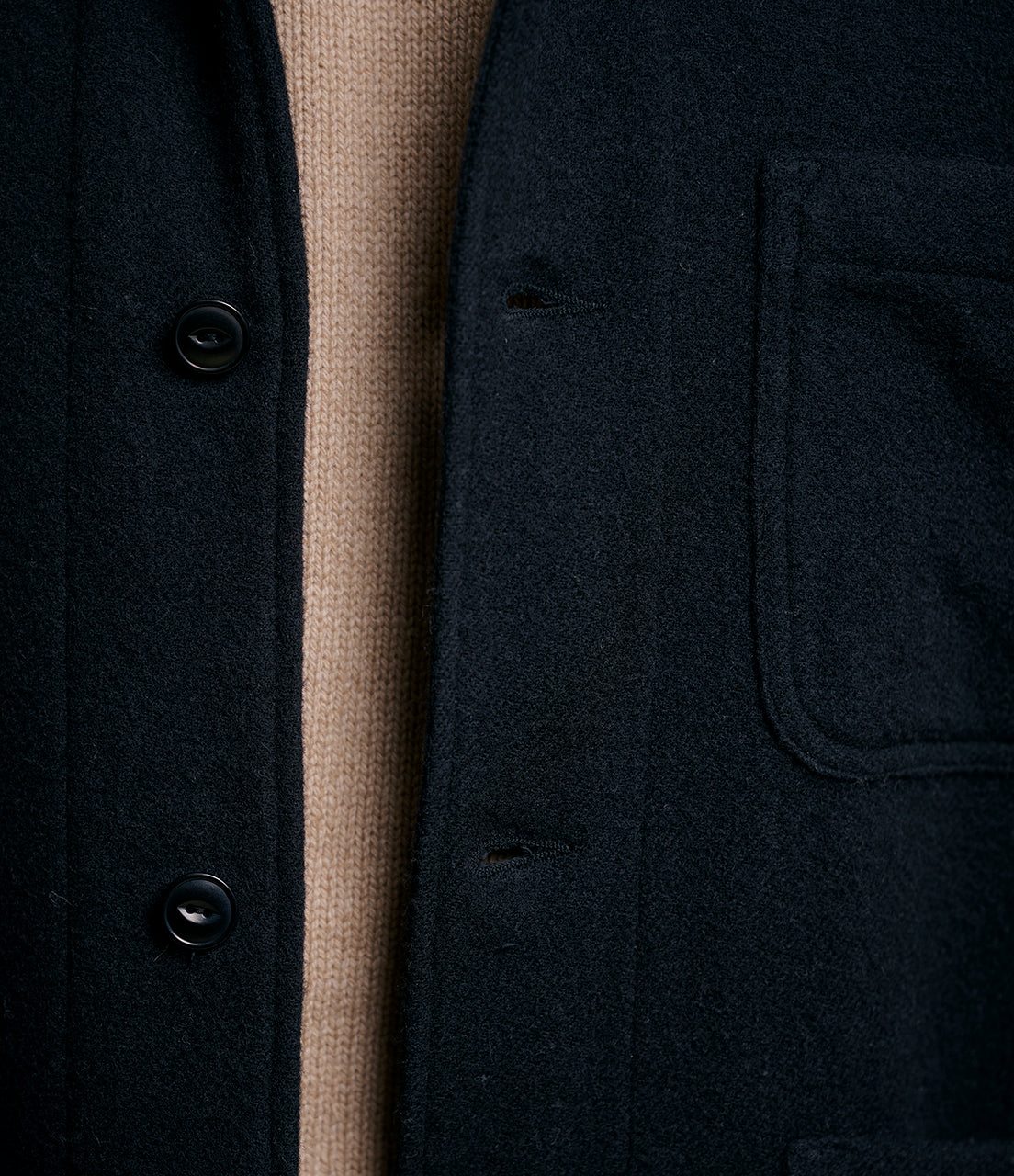 Close-up of a dark wool jacket with buttons and a pocket, showing a beige interior.