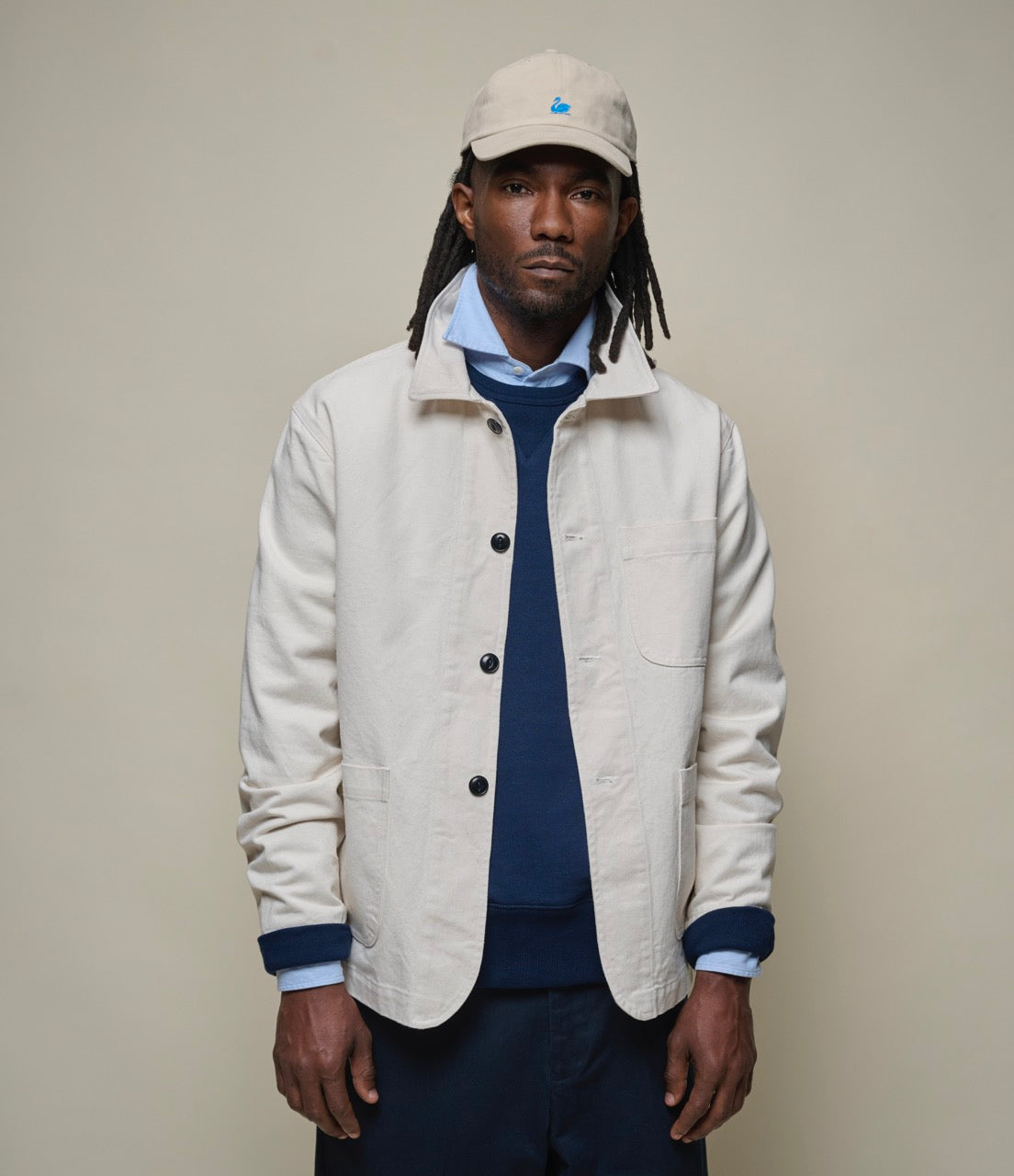 Man wearing a beige jacket and cap against a plain background