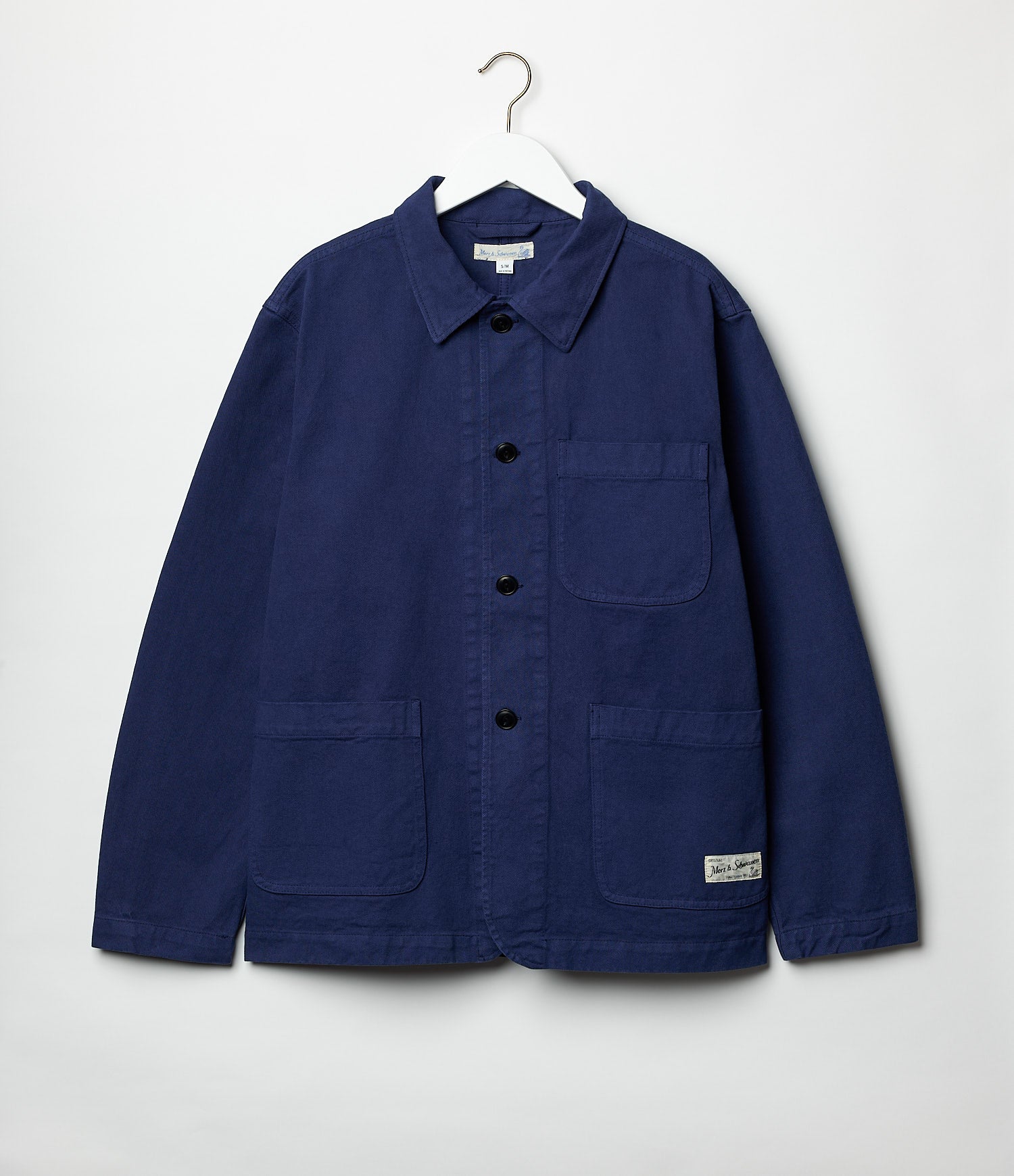 A blue cotton twill jacket with a collar, buttons, and pockets, displayed on a hanger against a white background.