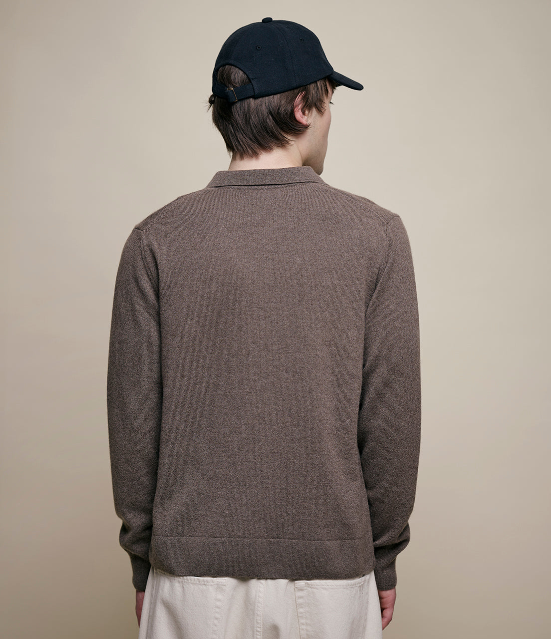 Person wearing a brown sweater and black cap against a plain background