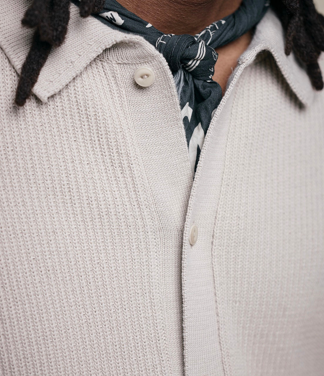 Close-up of a person wearing a light gray ribbed shirt with a patterned scarf around their neck.