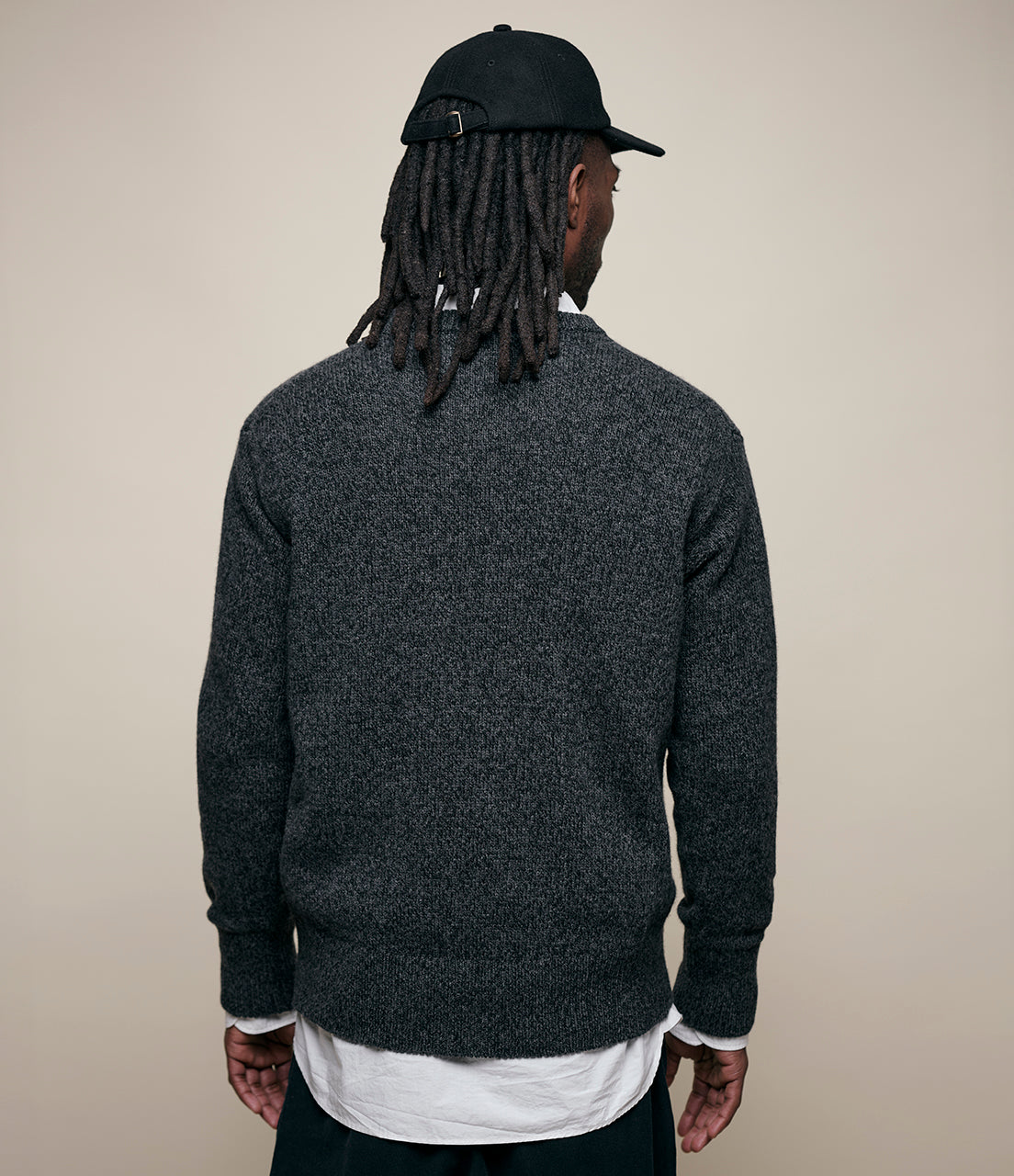 Person wearing a dark gray sweater and black cap from behind on a beige background
