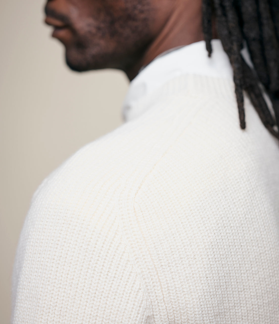 Person wearing a white sweater against a neutral background