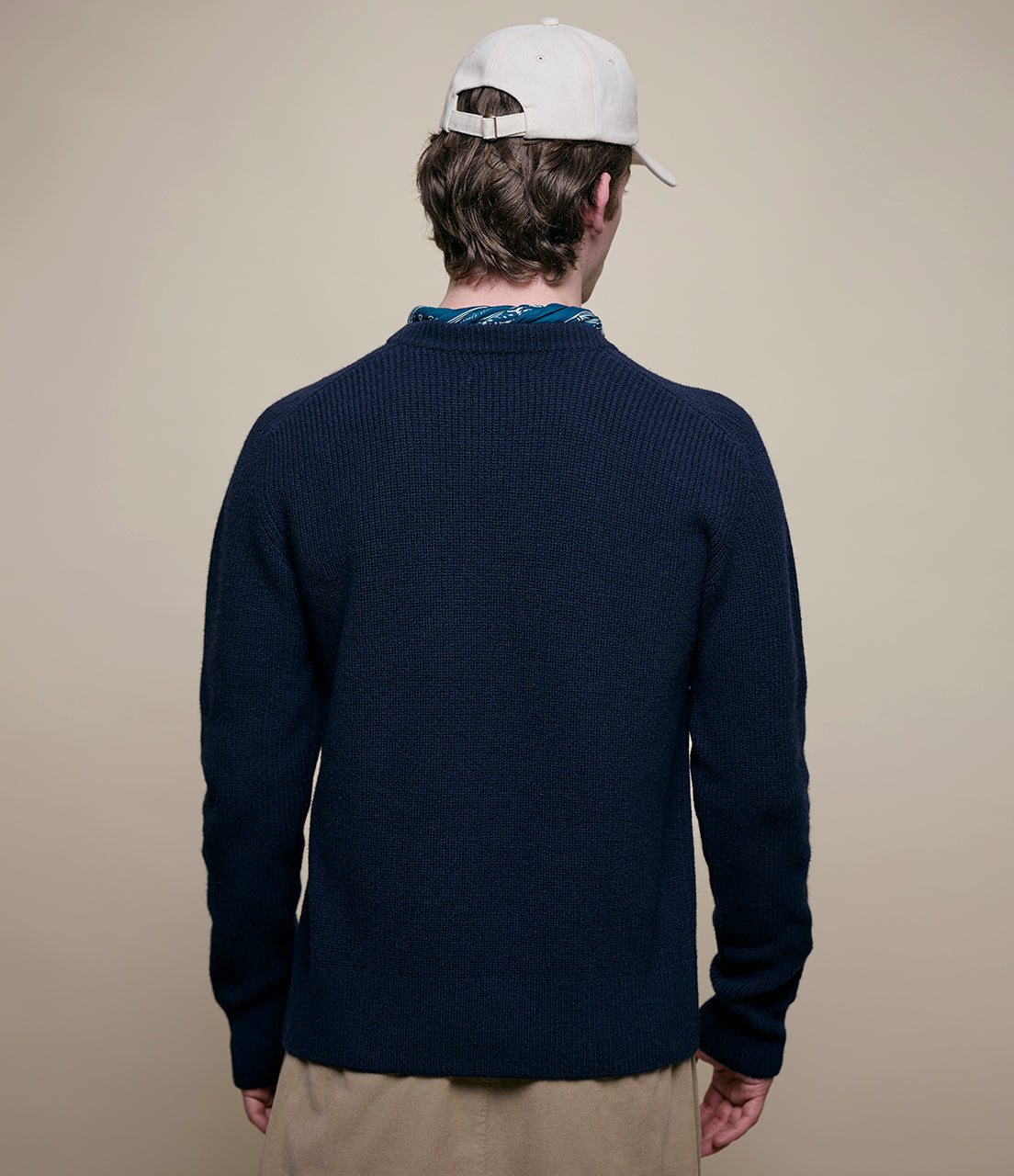 Person wearing a navy blue sweater and beige pants with a plain background