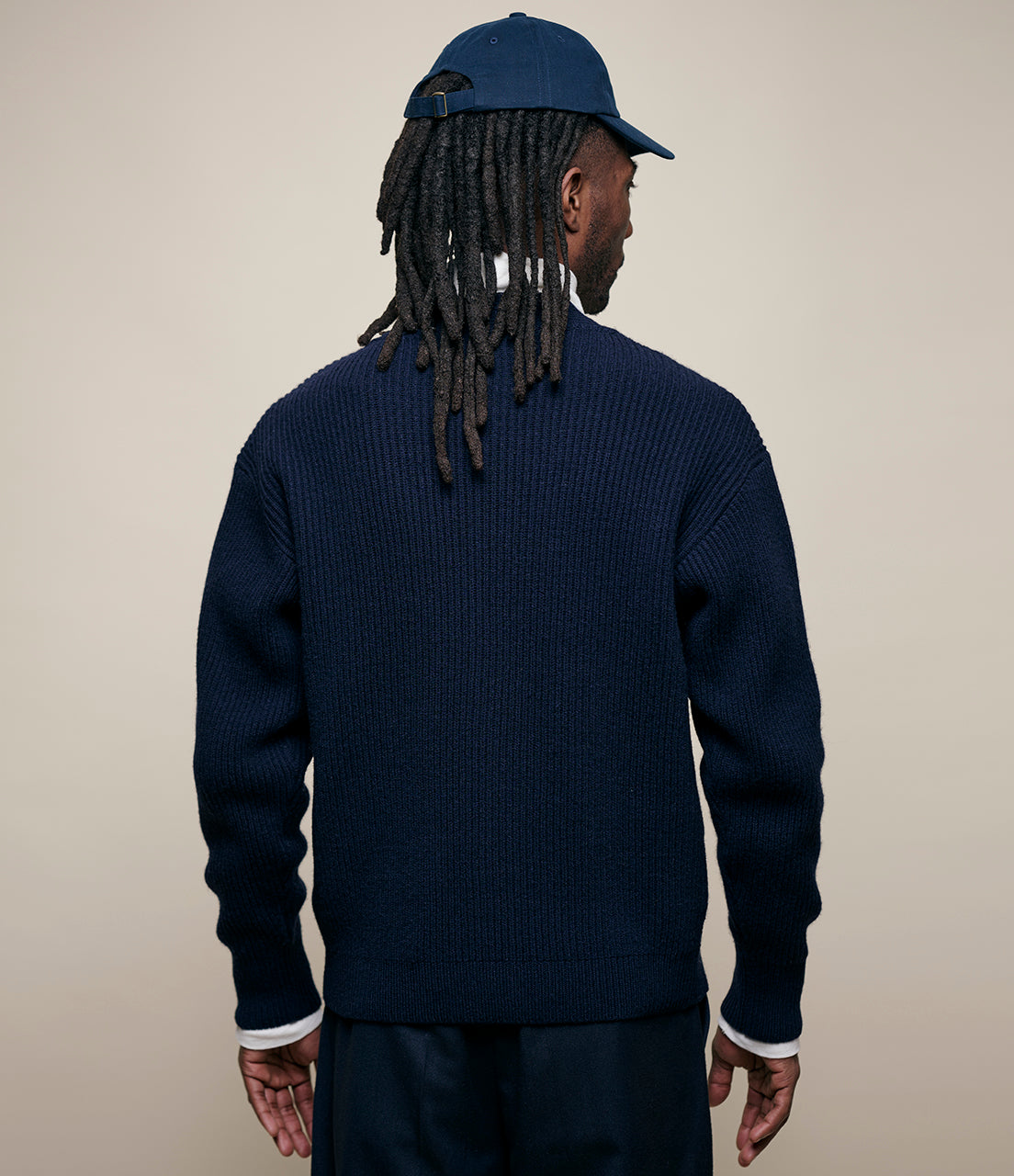 Person wearing a navy sweater and cap on a beige background