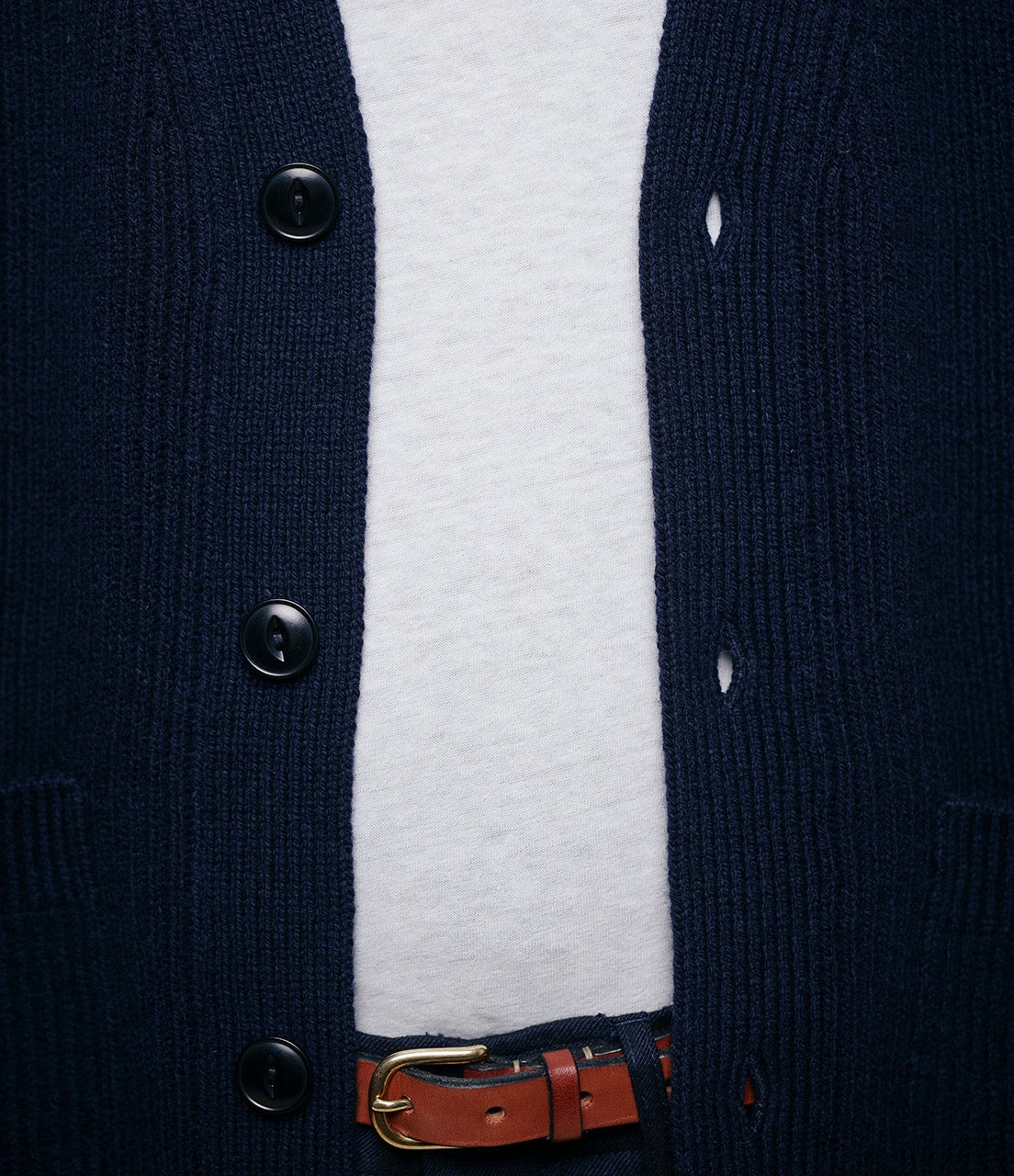 Navy cardigan with buttons and a white shirt underneath, featuring a brown belt.
