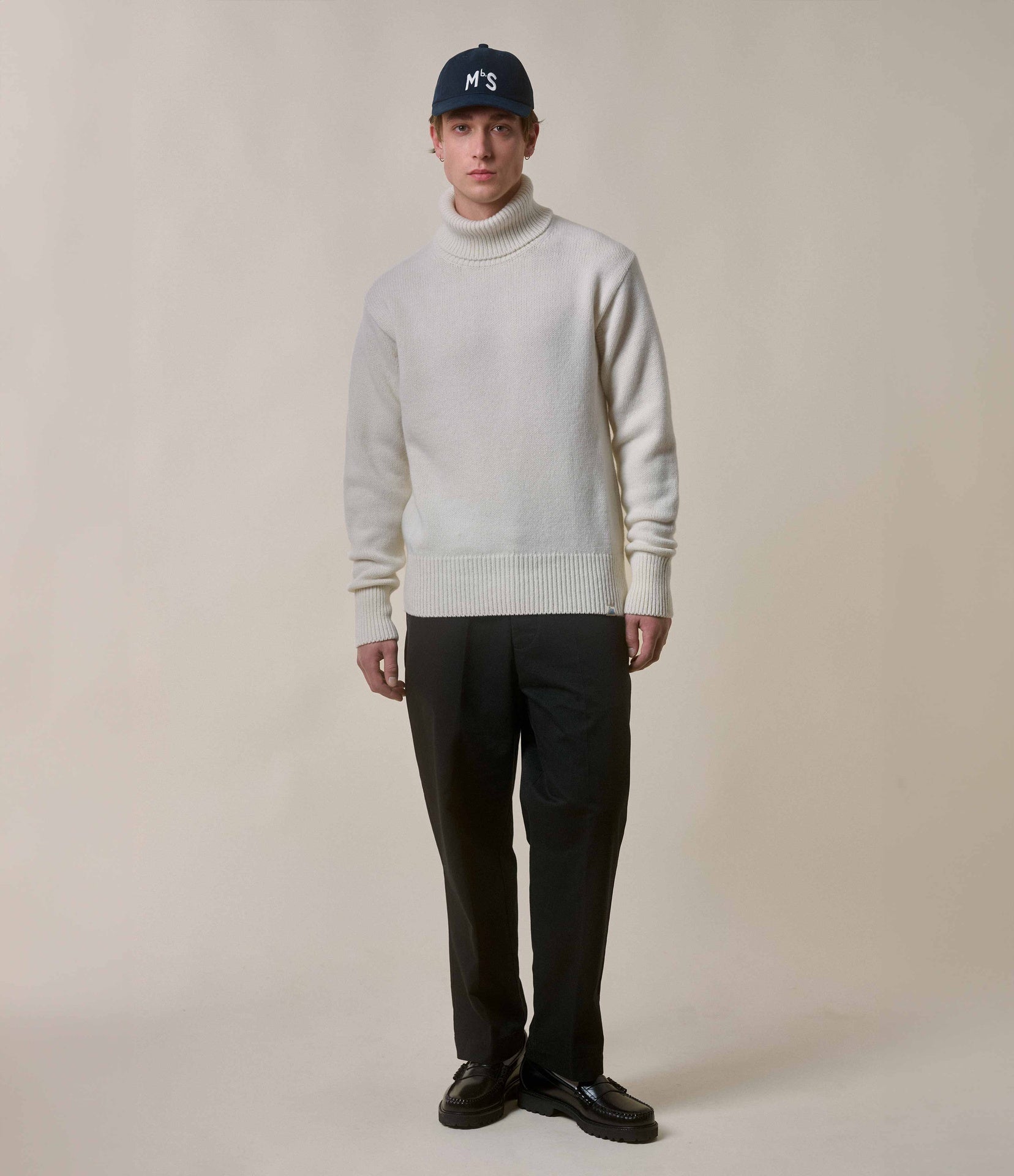 Person wearing a white sweater and black pants against a plain background