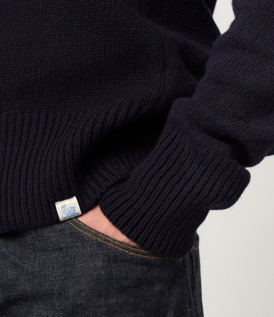 Person wearing a dark blue sweater with a brand logo on a light gray background