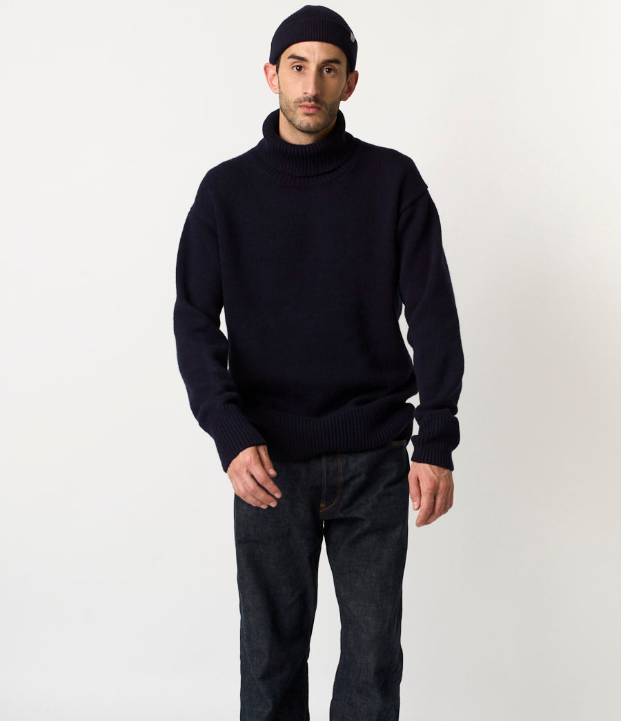Man wearing a black turtleneck sweater and dark pants on a white background