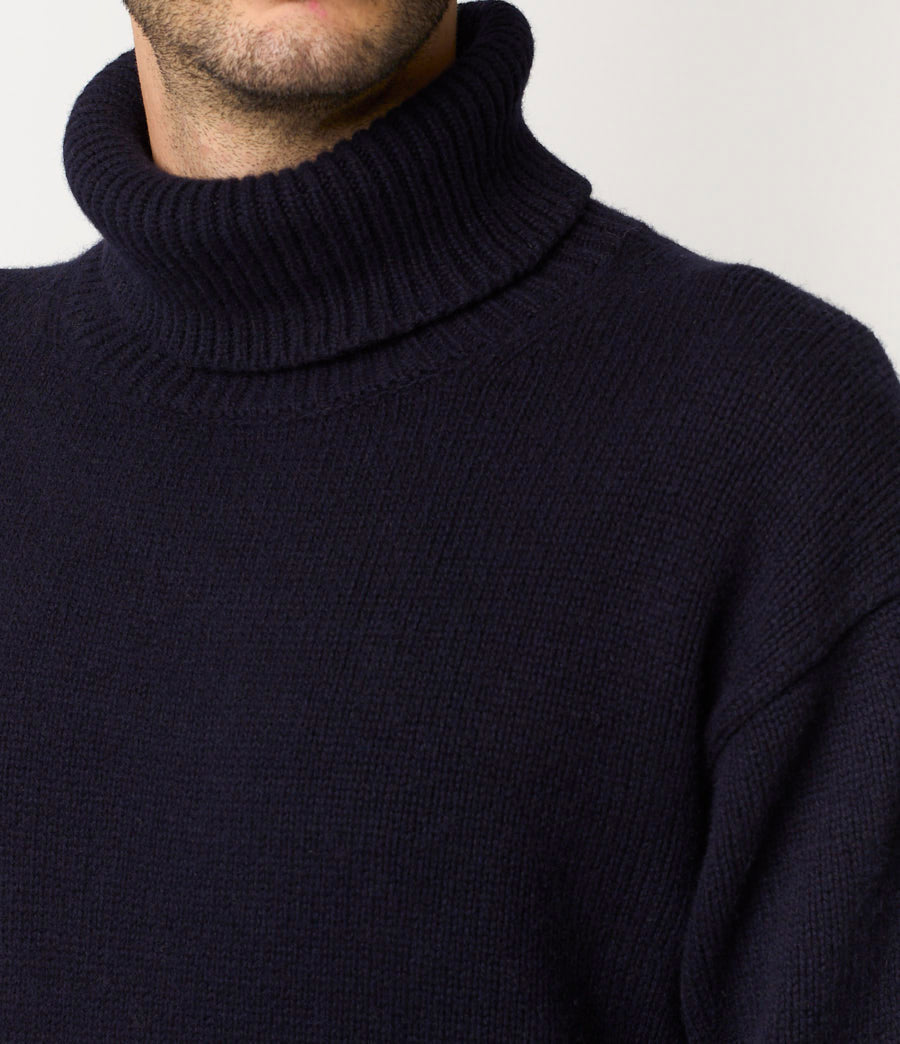 Navy blue turtleneck sweater worn by a person on a light gray background